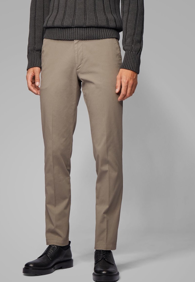 Chinos beige clair en coton, avec une coupe slim, une texture lisse et un design épuré, assortis à des chaussures en cuir noir.