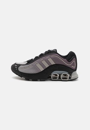 Chaussure de sport noire et grise avec tige en mesh, trois bandes horizontales et un design de talon rembourré distinctif. Bout arrondi et semelle texturée.