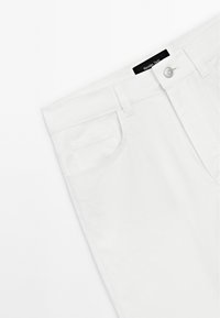 Vita bomullsbyxor med slät framdel, en enda ficka på vänster sida och en svart märkesetikett på midjebandet.