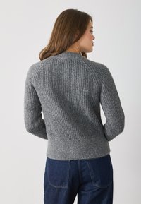 Gray ribbed sweater with long sleeves, round neckline, and a fitted waistband. The texture is soft and knit, offering a cozy appearance.