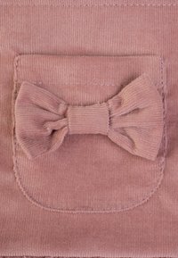 Teddy-Stofftasche in sanftem Rosa mit einem strukturierten Schleifendetail. Die Naht ist am Rand der Tasche sichtbar, was das Design hervorhebt.
