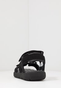 Czarne sandały z regulowanymi paskami, fakturowanym wkładką i elastyczną gumową podeszwą. Widok z tyłu podkreśla otwarty dizajn i miękkie materiały.