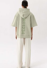 Oversized lichtgroene hoodie met capuchon, met een bedrukte verticale ontwerp op de achterkant. Gepaard met losse crèmekleurige broeken.