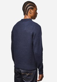 Navy Wollpullover mit geripptem Rundhals- und Bündchen. Strukturiertes Material, taillierte Ärmel und dezente Stickdetails an den Schultern.