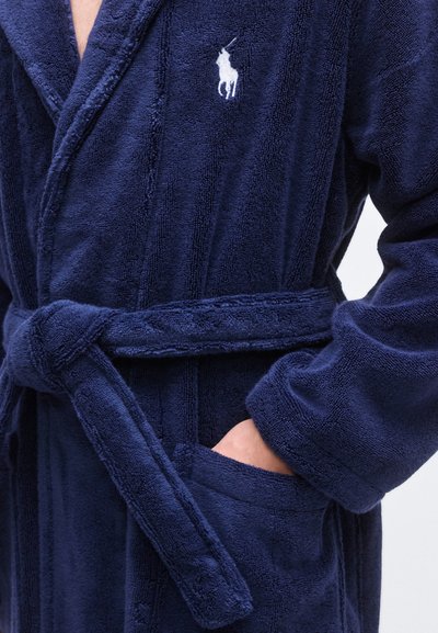 Mørkeblå badekåpe i frotté med sjalskrage, midjebånd, lappelomme og en liten brodert logo på brystet. Myk tekstur.