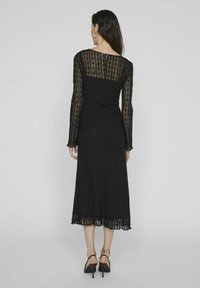 Melnas mežģīņu kleitas ar garām piedurknēm, pieguļošu augšu un platu svārku ar viļņotu apakšmalu. Audumam ir izteikta tekstūra.