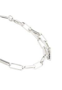 Hõbedane metallist ketiprääk, millel on ovaalsed lingid ja väike silt, millel on graveeritud "PILGRIM". Sile tekstuur ja poleeritud viimistlus.