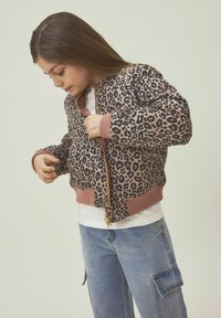 Bomberjack met luipaardprint en een gouden ritssluiting, aansluitende manchetten en geribde onderkant. Draag het over een wit T-shirt en combineer het met lichtblauwe cargo-jeans.