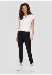 Witte linnen blouse met korte opgerolde mouwen, gecombineerd met zwarte slim-fit cargobroek met zijzakken en een knoopsluiting. Witte sneakers.