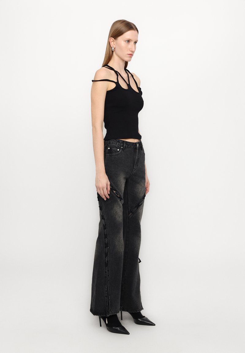Top nero senza maniche con aperture, abbinato a jeans in denim neri a vita alta con cerniere laterali e orli grezzi, completato con tacchi a stiletto.