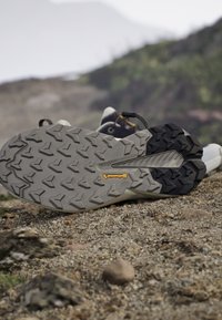 Semelle de chaussure de randonnée avec des profils profonds et le logo Continental reposant sur un terrain rocheux avec un paysage naturel flou en arrière-plan.