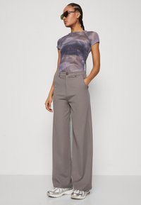Gray wide-leg pants with a button closure and side pockets, paired with a short-sleeve, multicolored tie-dye top and silver sneakers.