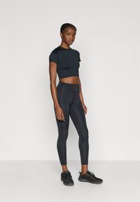 Sort, beskåret atletisk top kombineret med højtsiddende sorte leggings. Modellen bærer sorte sneakers. Glat, elastisk stof over det hele.