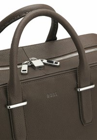 Malette en cuir marron avec finition texturée, deux poignées supérieures, quincaillerie en acier inoxydable et fermeture à glissière. Présente également un logo 'BOSS' en relief sur le côté.