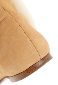 Gros plan du talon d'une chaussure en daim beige avec des coutures visibles et une semelle en cuir marron sur fond blanc.