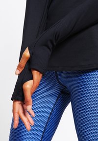 Svart långärmad topp med tumhål, kombinerad med blåmönstrade leggings som har en geometrisk textur och kontrasterande svarta sömmar.