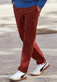 Rode katoenen broeken met opgerolde manchetten, gecombineerd met witte en grijze sneakers met zwarte accenten. Gedragen over een blauwe gebreide trui.