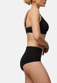 Sujetador negro y braguitas de talle alto hechas de tela suave. El sujetador cuenta con tirantes ajustables y un borde con puntillas, garantizando comodidad y un buen ajuste.