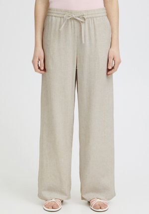 Pantaloni largi din in, bej, cu talie elastică și șnur, purtați cu sandale albe cu bretele, arătați pe o persoană în picioare.