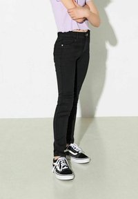 Černé úzké džíny z denimu, s mírně zvýšeným pasem, s drobným opotřebením a designem s pěti kapsami, kombinované s černobílými teniskami.