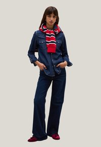 Camisa de mezclilla con botones a presión, combinada con jeans acampanados de color azul oscuro. Un suéter a rayas rojo y blanco atado al cuello. Calzado rojo con borlas.