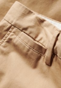 Pantalones cortos de tela marrón con una textura suave, un bolsillo trasero con bordes cosidos y un lazo para ajustar en la cintura.