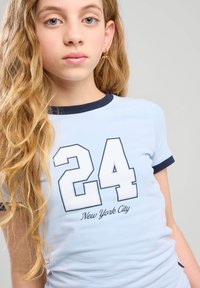 Vaaleansininen lyhythihainen t-paita, jossa on tummansininen ribbikaulus. Edessä on suuri valkoinen numero "24" ja "New York City" -teksti painettuna alle. Pehmeä pinta.