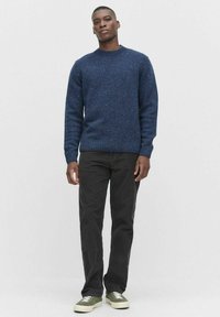 Tummansininen neulepaita, jossa on tekstuuripinta ja ribattu kaula-aukko, yhdistetty mustiin housuihin ja oliivinvihreisiin lenkkareihin.