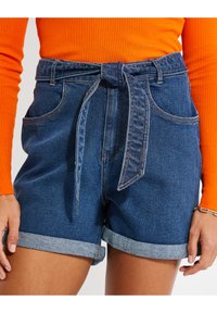Pantalones cortos de denim en azul oscuro con una cinturilla atada y puños enrollados. Cuenta con dos bolsillos laterales y costuras en contraste.
