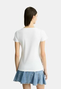 T-shirt bianco a maniche corte con scollo rotondo, abbinato a una gonna in denim a strati con orlo svasato e cuciture visibili.