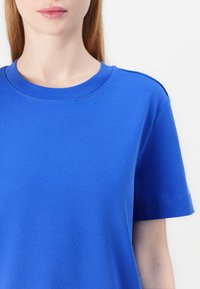 Lys blå kortärmad t-shirt med rund halsringning, mjuk bomullstextur och enkel design. Har axelsömmar med minimal sömnad.