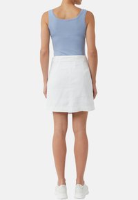 Helles blaues Tanktop kombiniert mit einem weißen Leinen-Minikleid. Der Rock hat einen flachen Bund und ist am Saum leicht ausgestellt.