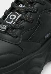 Sorte plattform sneakers laget av glatt materiale, med sorte lisser med hvit søm og "Buffalo" logo på siden. Krummet såledesign.