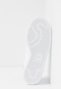 Vit sneakersula med ett hexagonmönster. Har en central logotyp vid hälen och en slät, platt design.