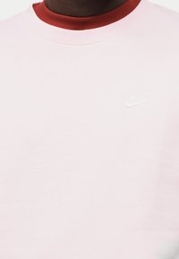 Sweatshirt cor de rosa clara com decote redondo e gola contrastante em bordô. Pequeno logotipo branco da Nike no peito. Textura macia do tecido.