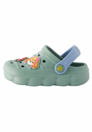 Bocassins vert clair avec une semelle surélevée, ornés de charms de personnages de dessin animé et de trous de ventilation. Une sangle bleue ajustable à l'arrière.