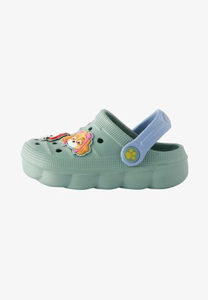Light green clogs with a raised sole, featuring cartoon character charms and ventilation holes. Blue adjustable strap at the back.