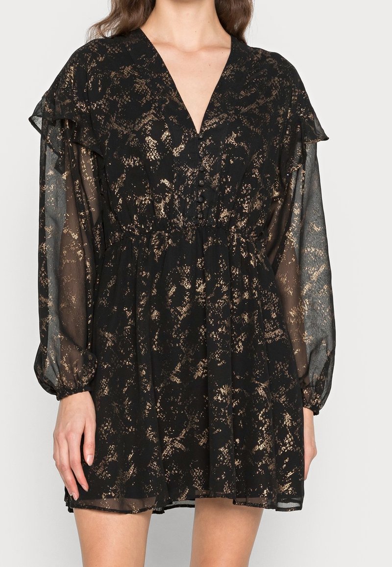 Robe noire avec motif en feuille d'or, manches longues transparentes, col en V, devant boutonné et détail à volants sur les épaules.