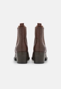 Bottines en cuir marron avec une finition lisse, panneaux latéraux élastiques et un talon en bois sombre texturé, dotées de languettes à l'arrière pour un enfilage facile.