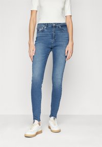 Jeans de denim azul ajustados con cintura de media altura, diseño de cinco bolsillos y un ligero desgaste, combinados con zapatillas blancas.