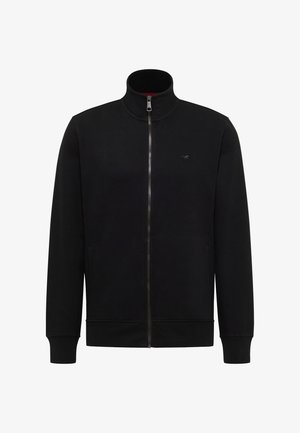 Juoda striukė su užtrauktuku visame ilgyje, stovinčiu apykakliu, rištu rankogaliu ir apačia, dvi šoninės kišenės ir maža išsiuvinėta logotipas krūtinės srityje.