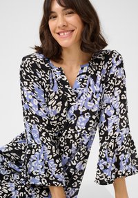 Schwarzes Kleid mit blau-weißer Leopardenmusterung, V-Ausschnitt und ausgestellten Ärmeln, aus leichtem, strukturiertem Stoff.