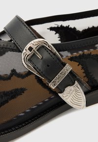 Black mesh sandal featuring a textured brown pattern, silver metal buckle with ornate detailing, and sturdy sole with contrast stitching.