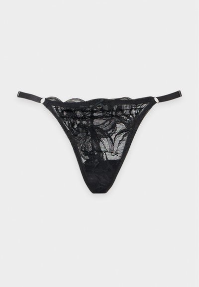 String en dentelle noire avec bretelles latérales réglables et motif en maille florale sur un fond uni clair.
