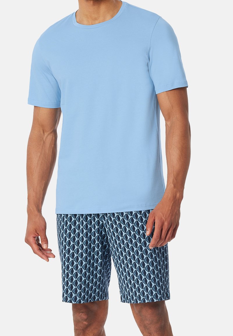 Světle modré bavlněné tričko s kulatým výstřihem spojené s námořnickými šortkami se vzorem obsahujícím geometrické tvary v různých odstínech modré.