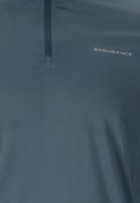 Lättvikts blå atletisk skjorta med halvdragkedja, texturerad tyg och varumärket "ENDURANCE" tryckt i vitt på sidan.