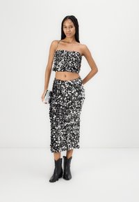 Top corto de lentejuelas negras y plateadas con falda larga a juego, acompañado de botas de tobillo negras. Textura suave y brillante con diseño en capas.