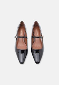 Des chaussures Mary Jane en cuir verni noir avec des orteils carrés et de fines brides à boucle, présentées de dessus sur un fond blanc.