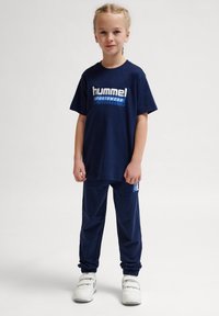 Marineblåt sportstøjssæt, der indeholder en t-shirt med det iøjnefaldende "hummel" logo og matchende bukser med elastiske manchetter og et ekstra logodetalje.