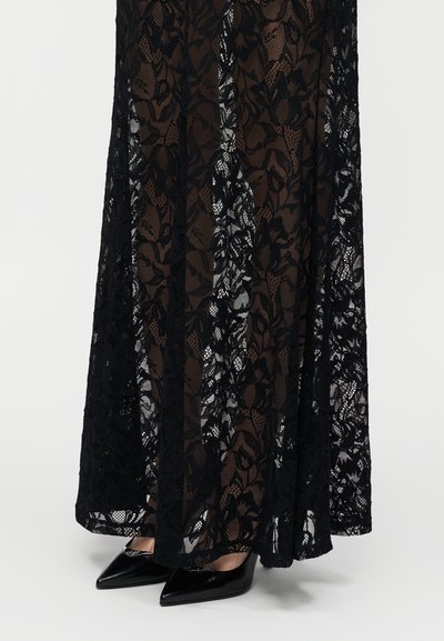 Ilgas juodas nėrinių sijonas su gėlių raštais ir permatomomis panelėmis. Segimas su aštrokomis juodomis aukštakulnėmis, demonstruojančiomis subtilią tekstūrą ir dizainą.